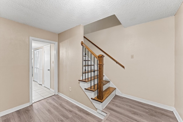 stairs with a textured ceiling, baseboards, and wood finished floors