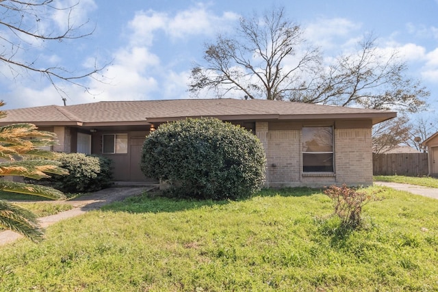 view of front of home featuring brick siding, fence, a front lawn, and roof with shingles