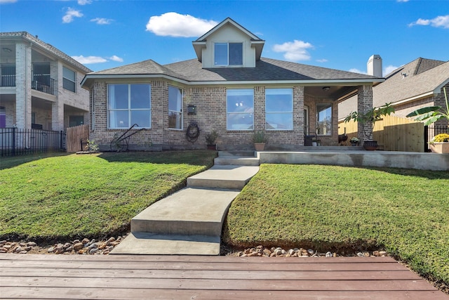 view of front of property with a front yard, brick siding, fence, and roof with shingles