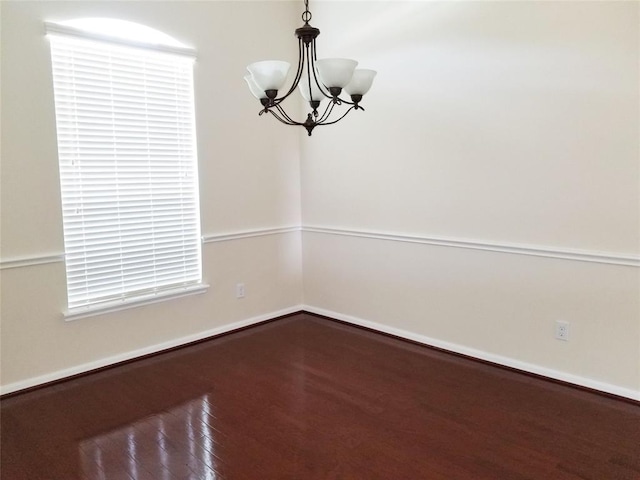 spare room featuring wood finished floors, baseboards, and an inviting chandelier