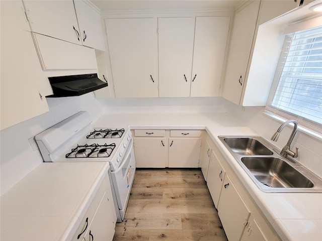 kitchen with tile countertops, white gas stove, under cabinet range hood, and a sink