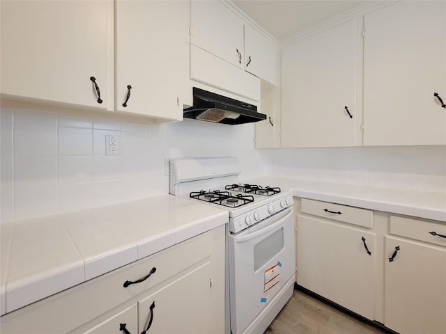 kitchen with white gas stove, white cabinets, tasteful backsplash, and under cabinet range hood