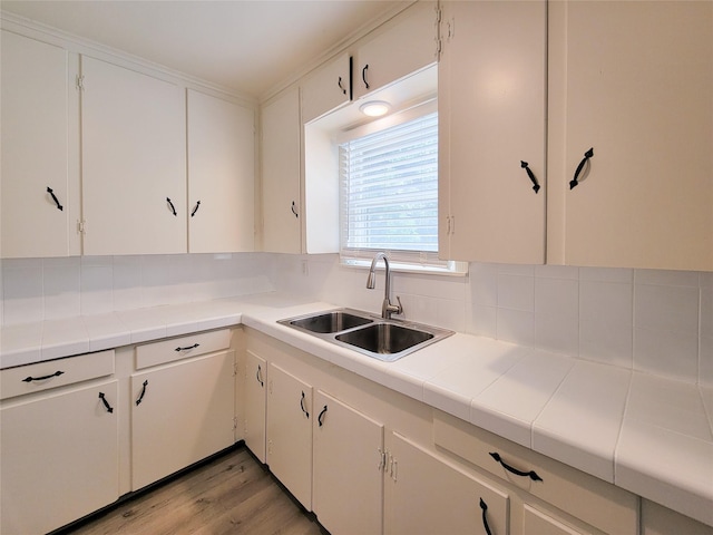 kitchen with white cabinetry, light wood-style flooring, tile countertops, and a sink