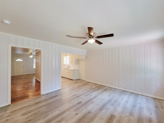 unfurnished living room with a sink, ornamental molding, light wood finished floors, and ceiling fan