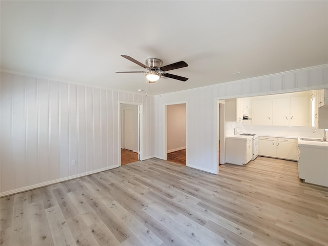 unfurnished living room featuring a ceiling fan, a sink, crown molding, light wood finished floors, and baseboards