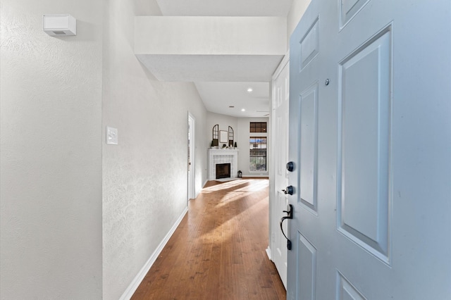 corridor with recessed lighting, a textured wall, baseboards, and wood finished floors