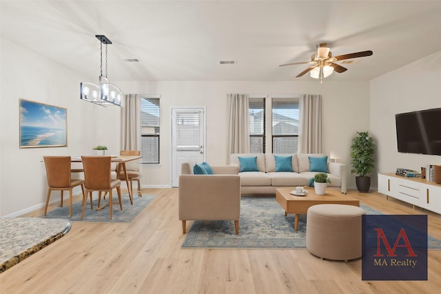 living area with ceiling fan with notable chandelier, light wood-type flooring, visible vents, and baseboards