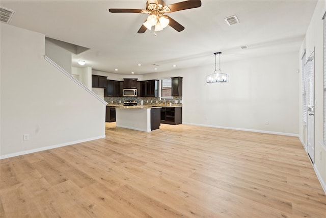 unfurnished living room featuring light wood-style floors, baseboards, visible vents, and ceiling fan with notable chandelier