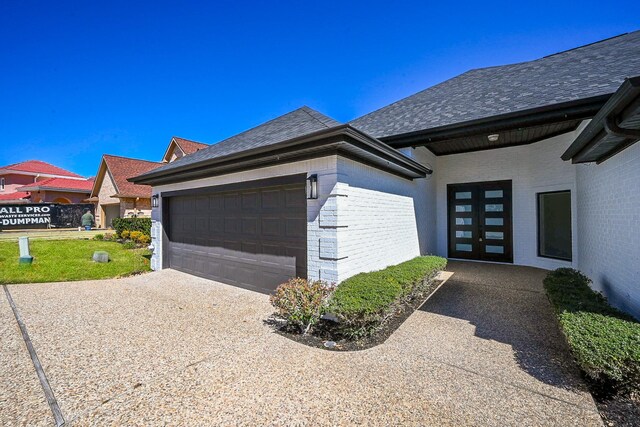 view of side of home featuring a shingled roof, brick siding, and an attached garage