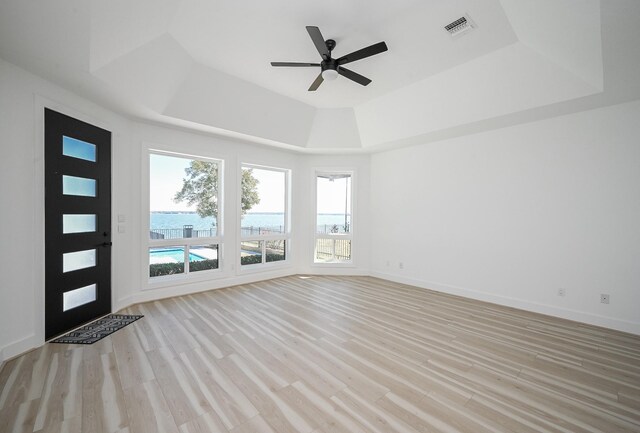 interior space featuring baseboards, visible vents, light wood-style flooring, ceiling fan, and a tray ceiling