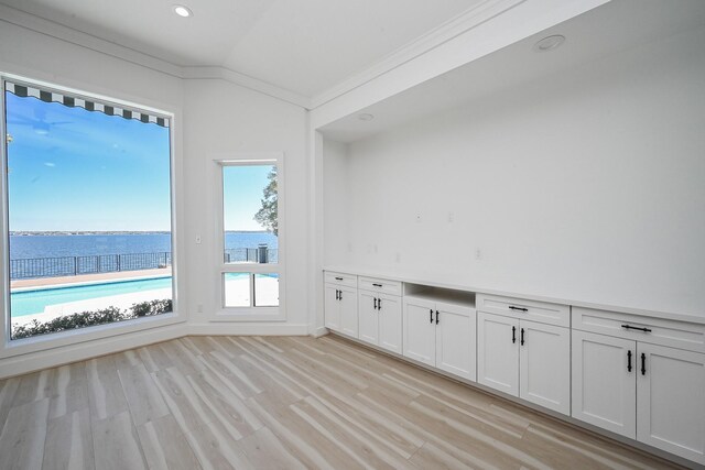 empty room featuring lofted ceiling, a water view, crown molding, light wood-style floors, and recessed lighting