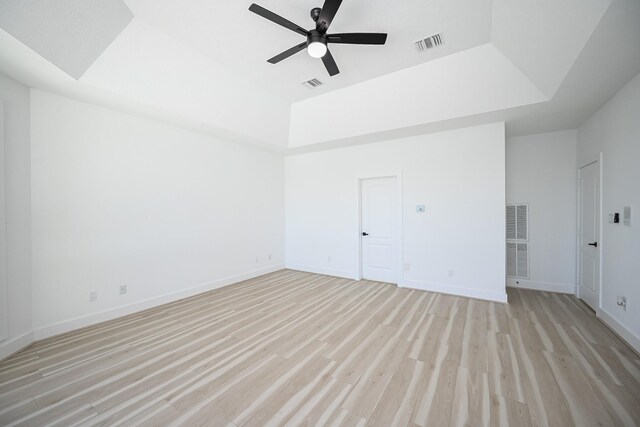 empty room featuring light wood-style floors, visible vents, and a raised ceiling