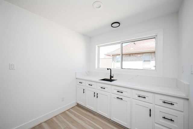 interior space with a sink, white cabinetry, light wood-style floors, baseboards, and light stone countertops