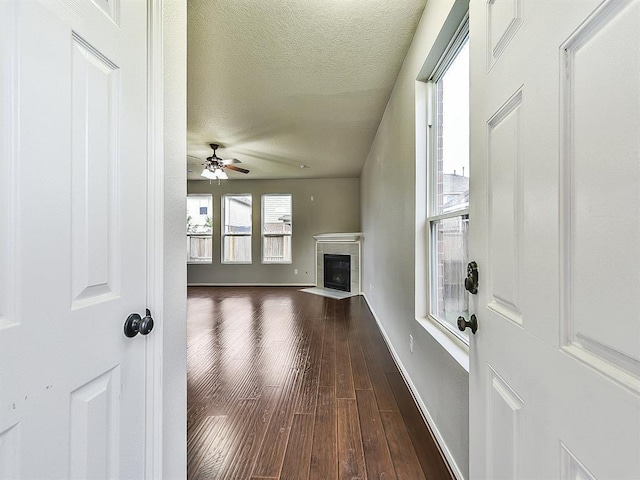 unfurnished living room featuring dark wood-style floors, ceiling fan, a textured ceiling, a tile fireplace, and baseboards