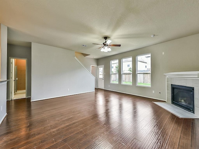 unfurnished living room with dark wood-style flooring, a fireplace, visible vents, ceiling fan, and a textured ceiling