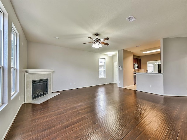 unfurnished living room with ceiling fan, a fireplace, dark wood finished floors, and visible vents