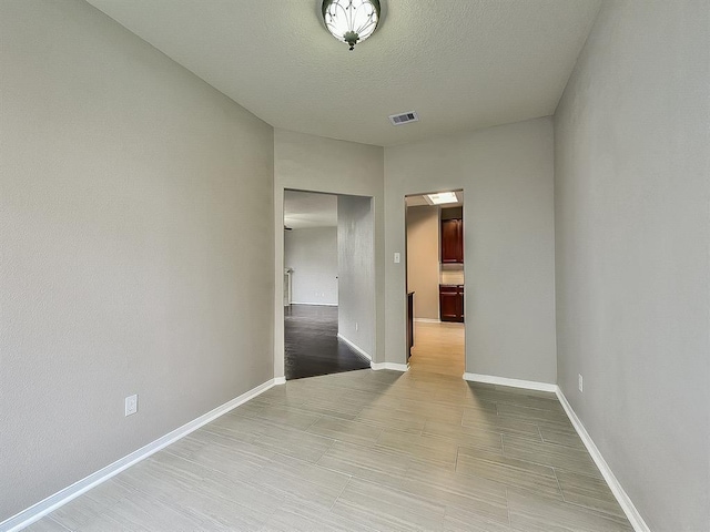 empty room featuring visible vents, a textured ceiling, and baseboards