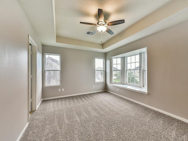 empty room featuring a textured ceiling, carpet floors, a tray ceiling, and baseboards