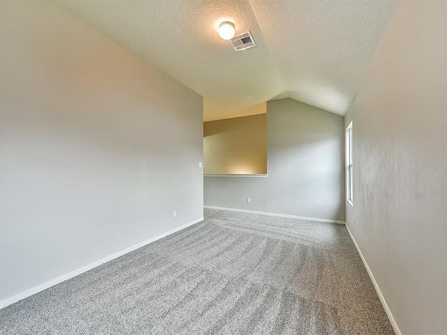 carpeted empty room featuring visible vents, vaulted ceiling, a textured ceiling, and baseboards