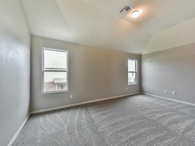 carpeted empty room with lofted ceiling, visible vents, a textured ceiling, and baseboards