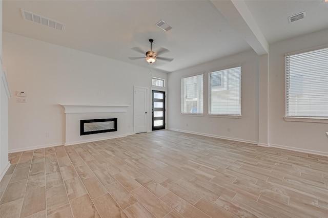 unfurnished living room with light wood-style flooring, a glass covered fireplace, visible vents, and baseboards