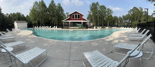 community pool with an outbuilding, a storage unit, a patio area, and fence