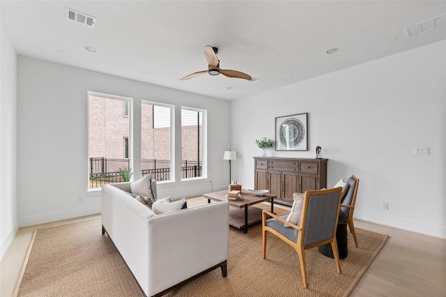 living room featuring light wood finished floors, a ceiling fan, visible vents, and baseboards