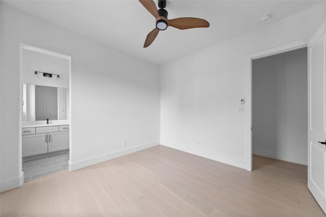 unfurnished bedroom featuring light wood finished floors, ensuite bathroom, ceiling fan, a sink, and baseboards