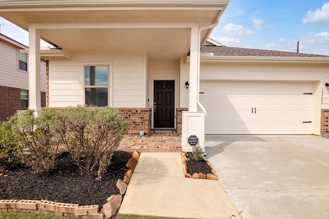 view of exterior entry with driveway, brick siding, roof with shingles, and an attached garage