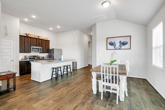 kitchen with an island with sink, dark brown cabinetry, stainless steel appliances, and dark wood-type flooring