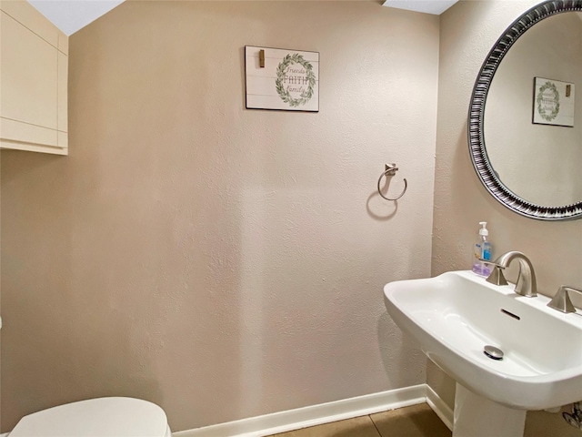 half bathroom with toilet, tile patterned flooring, baseboards, and a sink