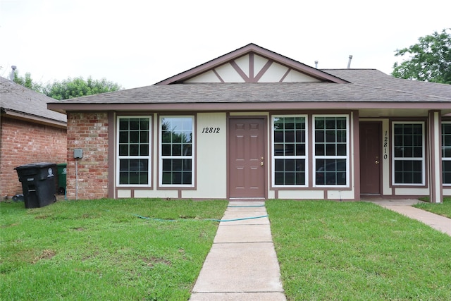 view of front of property with a shingled roof, a front yard, brick siding, and stucco siding