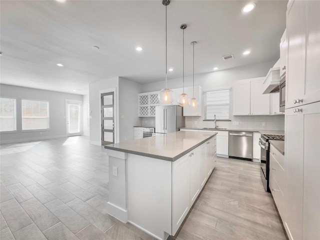 kitchen with a sink, white cabinetry, appliances with stainless steel finishes, a center island, and tasteful backsplash