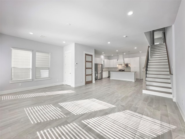 unfurnished living room featuring light wood-style floors, stairs, baseboards, and recessed lighting