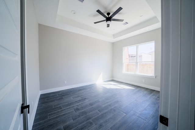 unfurnished room with a tray ceiling, dark wood-style flooring, visible vents, and a ceiling fan