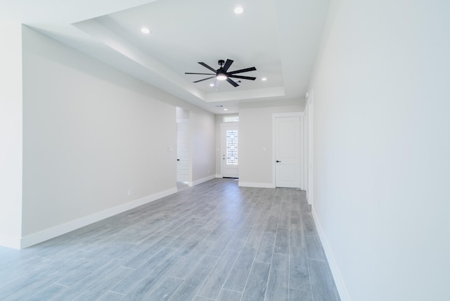 spare room featuring light wood finished floors, baseboards, ceiling fan, a tray ceiling, and recessed lighting