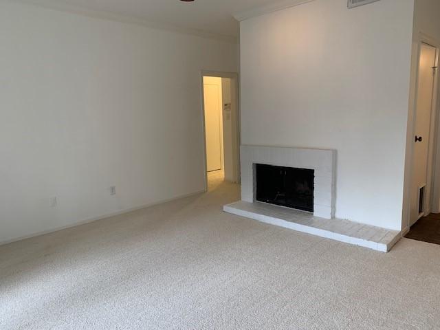 unfurnished living room featuring carpet floors, a brick fireplace, visible vents, and crown molding