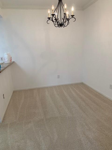 carpeted empty room featuring ornamental molding, baseboards, and an inviting chandelier