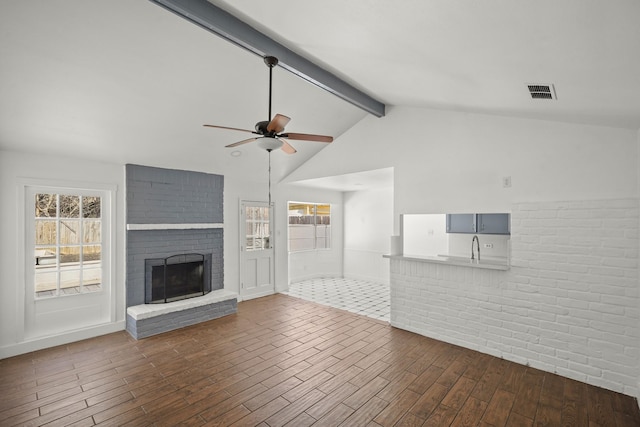 unfurnished living room with a fireplace, visible vents, a ceiling fan, wood finished floors, and beamed ceiling