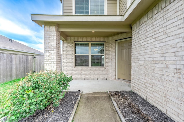 doorway to property with brick siding and fence