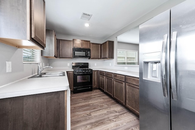 kitchen featuring light wood-style flooring, dark brown cabinetry, a sink, visible vents, and black appliances