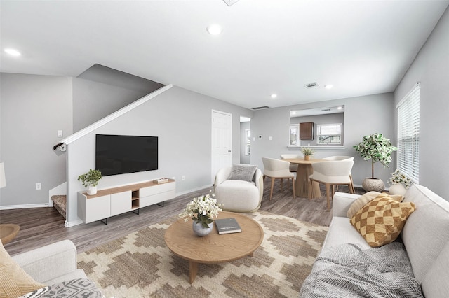 living room featuring stairway, baseboards, visible vents, and wood finished floors