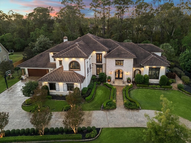 mediterranean / spanish-style house featuring a tiled roof, decorative driveway, a chimney, and a front yard