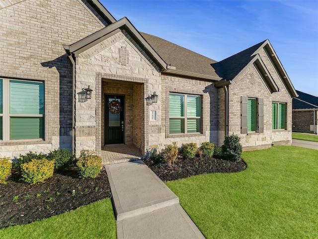 view of front of home featuring stone siding, brick siding, roof with shingles, and a front yard