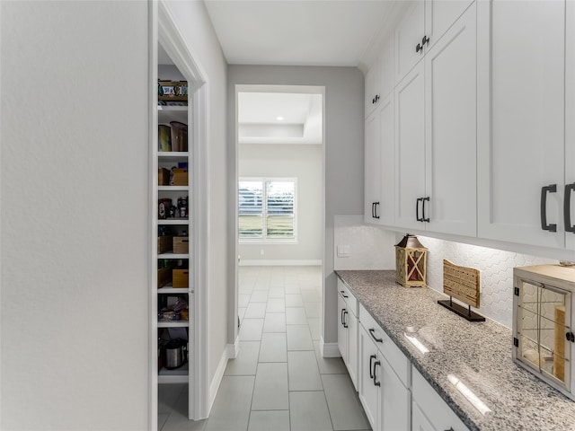 kitchen featuring light tile patterned floors, tasteful backsplash, white cabinets, light stone countertops, and baseboards