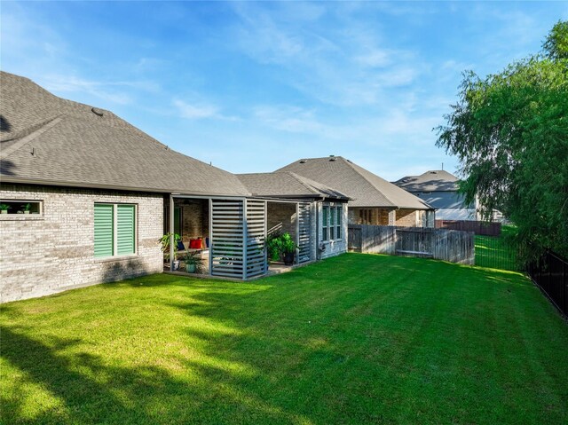 rear view of property with roof with shingles, brick siding, a lawn, and fence