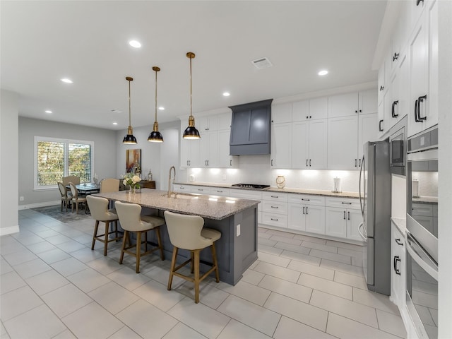 kitchen with a breakfast bar area, a sink, backsplash, light stone countertops, and an island with sink