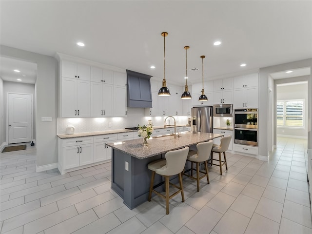 kitchen with decorative backsplash, appliances with stainless steel finishes, a kitchen island with sink, a sink, and a kitchen bar