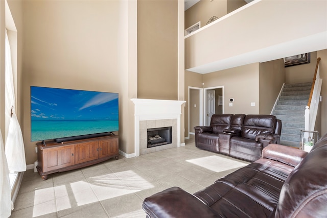 living area with light tile patterned floors, baseboards, a tile fireplace, stairs, and a high ceiling