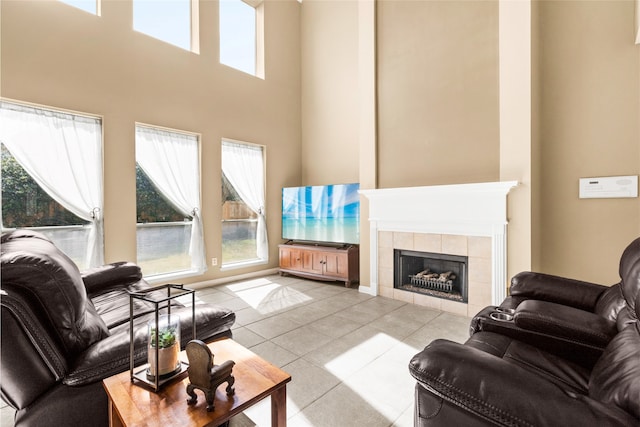 living room featuring a towering ceiling, light tile patterned floors, baseboards, and a tile fireplace